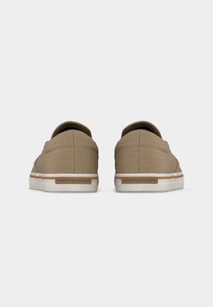 Paire de baskets beiges décontractées avec semelles blanches, vues de dos, avec une étiquette marron sur chaque talon.