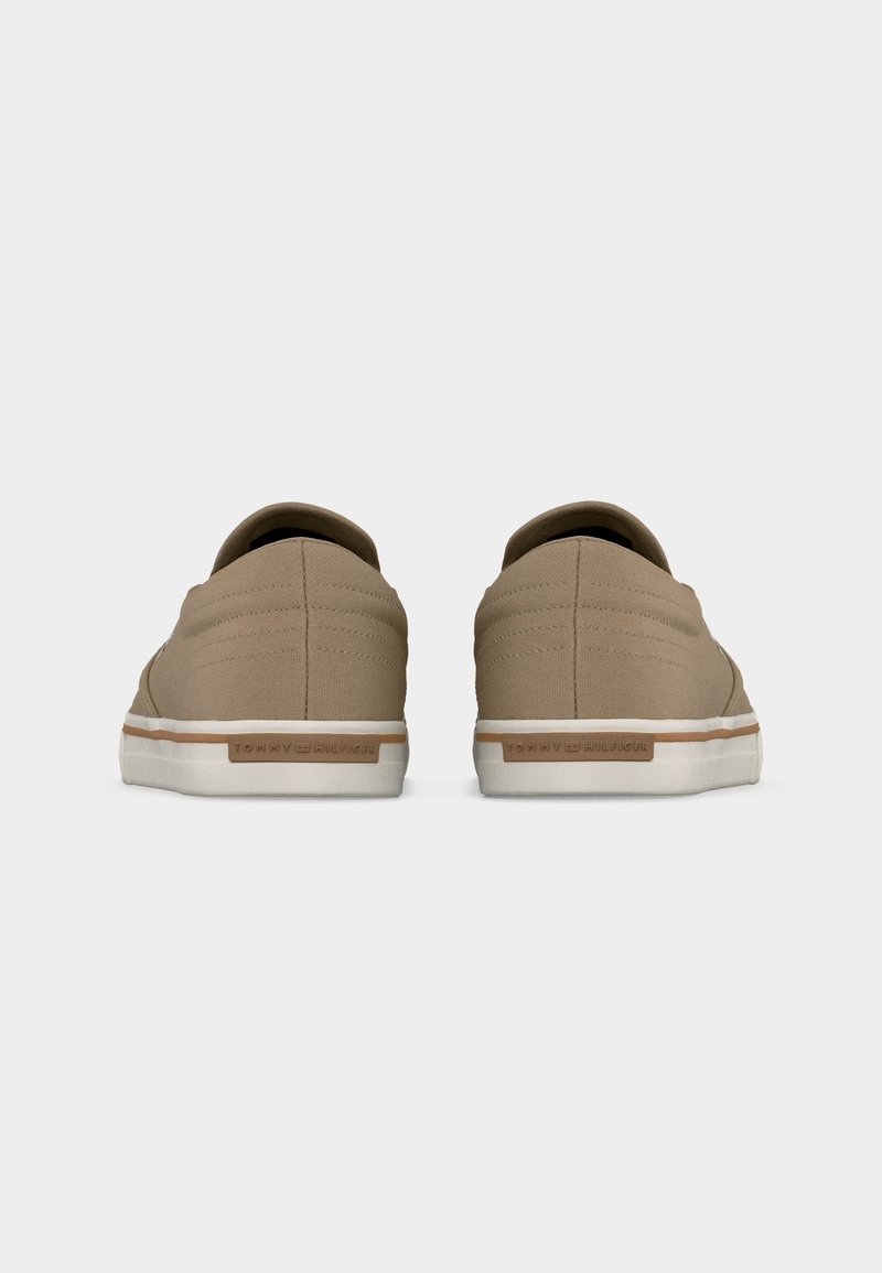 Paire de baskets beiges décontractées avec semelles blanches, vues de dos, avec une étiquette marron sur chaque talon.
