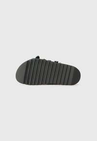Black sandal with a ridged rubber sole, featuring adjustable straps and a smooth upper material. The design is simple and functional.