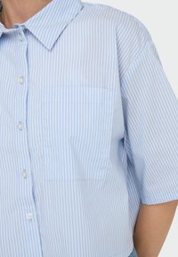 Camisa de manga corta a rayas azules y blancas, con un cuello clásico y un bolsillo en el pecho. Está hecha de una tela ligera con una textura suave.