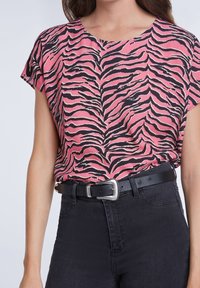 Haut à manches courtes rose avec un motif zébré noir, associé à un jean noir taille haute et une ceinture noire avec une boucle argentée.