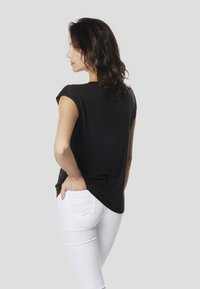 Melna īsroku krekla topi ar vaļīgu pieguļumu, kopā ar pieguļošām baltām džinsiem. Tops ir mīkstas tekstūras un ar smalkām mirdzošām akcentiem.