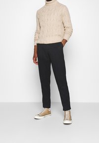 Krämfärgad kabelstickad polotröja, marinblå tapered byxor och beige högskor med vita sulor. Minimalistisk design, neutrala toner.