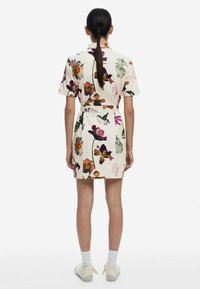 Sukienka z krótkim rękawem w kwiatowy wzór w różnych kolorach na kremowym tle. Posiada przewiązywany pas i sięga powyżej kolan. Gładka faktura.