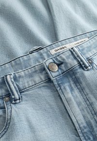 Világoskék farmernadrág fém gombbal és övbújtatókkal, a derékrészen egy „GABBA” feliratú fehér címkével.