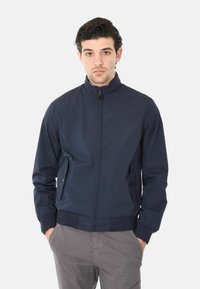 Giacca bomber leggera blu navy con colletto alto, chiusura con zip, due tasche laterali e polsini e orlo a coste. Texture liscia.