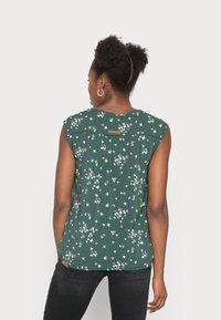 Blusa de manga curta verde-escura com padrão floral, apresentando pequenas borboletas em rosa e branco, com um leve plissado e detalhe de etiqueta nas costas.