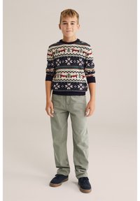 Stickad mönstrad tröja i marinblått, krämvitt och rött med renar och geometriska mönster. Matchas med ljusgröna byxor och marinblå skor.