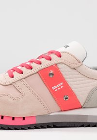 Zapatillas deportivas de ante rosa claro con un panel en color melocotón brillante. Presentan cordones rosas, detalles texturizados y una suela de goma gris. Marca visible en el lateral.