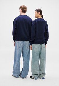 Námornícke bavlnené mikiny s opadávajúcimi ramenami v kombinácii s voľnými svetlomodrými a blednúcimi džínsami. Minimalistický dizajn s voľným strihom.