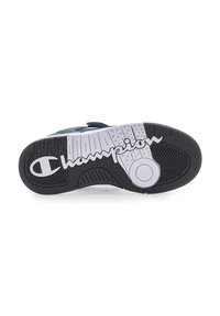 Suela de zapatilla deportiva en blanco y negro con patrones de agarre texturizados; presenta un corte circular y el logo de "Champion" exhibido de manera prominente.