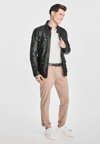 Czarna skórzana kurtka z zapinanymi kieszeniami, biała koszulka, beżowe spodnie, czarny pasek i białe trampki. Dopasowany krój z podwiniętymi mankietami.