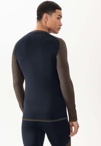 Haut de sport à manches longues avec un corps bleu marine et des manches marron. Confectionné en tissu lisse et extensible avec des accents contrastants et une coupe ajustée.