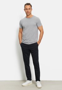 Maglietta grigia a maniche corte abbinata a pantaloni scuri. modello che indossa sneakers bianche. Tessuto liscio e design aderente.