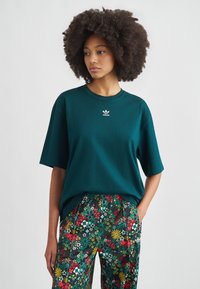 Türkis oversized t-shirt med korte ærmer og rund halsudskæring, med en lille hvid Adidas-logo. Kombineret med bukser med blomstertryk.