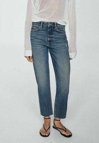 Jeans de denim azul con corte recto, ajuste a media altura, ligero desvanecimiento y diseño de cinco bolsillos, combinados con una blusa de punto blanca y sandalias negras.