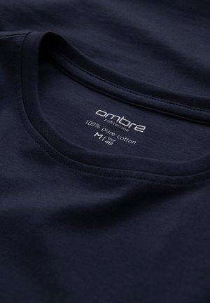 Camiseta azul marino hecha de 100% algodón puro, con cuello redondo y etiqueta con información de marca y tamaño. Textura suave.