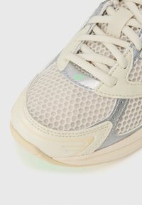 Baskets en mesh beige avec un accent argenté lisse, bout rond et semelle texturée avec lacets. Remarquables pour leur design supérieur respirant.