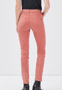 Vaqueros rosa de corte ajustado con cintura alta, con bolsillos traseros y detalles de costuras. Combinados con botines negros.