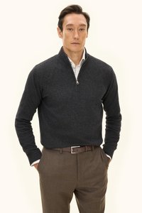 Dunkelgrauer Reißverschluss-Pullover aus Strickstoff mit Stehkragen und langen Ärmeln, kombiniert mit braunen Stoffhosen und einem Gürtel.