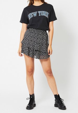 Zwarte t-shirt met "NEW YORK" in wit en blauw gedrukt, gecombineerd met een zwarte bloemenrok met ruffles en zwarte veterboots tot de enkels.