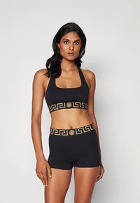 Μαύρο σετ αθλητικού crop top και σορτς, με χρυσό μοτίβο ελληνικού κλειδιού στις ζώνες, φτιαγμένο από λεία, ελαστική ύλη.