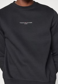 Felpa nera realizzata in tessuto misto cotone. Presenta un collo rotondo e un piccolo logo bianco con accento rosso sul petto.