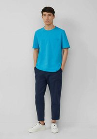 Turquoise short-sleeve T-shirt with a pocket, paired with navy tapered pants and white sneakers with black accents. Minimalist design.