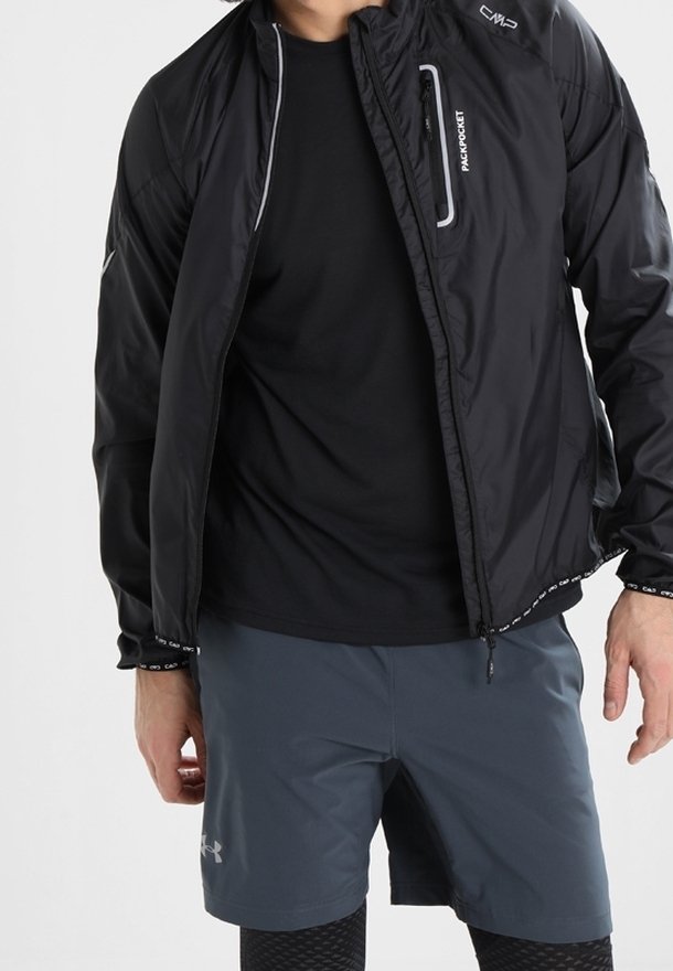 Veste noire légère avec une poche poitrine zippée, associée à une chemise noire et un short gris. La veste est dotée d'accents réfléchissants.