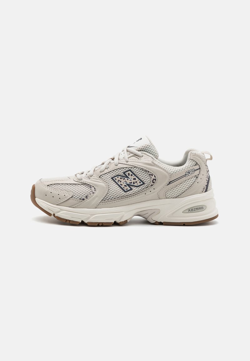Hellbeige Sporteschuh mit Mesh-Obermaterial, gepolstertem Kragen, strukturierten Akzenten und brauner Gummisohle; verfügt über das "N"-Logo an der Seite.