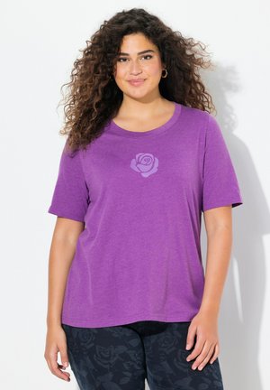 Camiseta corta de manga corta en color púrpura con un gráfico de rosa en el pecho. Tela suave con un corte holgado y cuello redondo, combinada con pantalones oscuros de estampado.