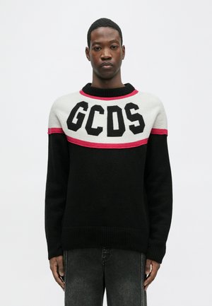 Black knitted sweater featuring a white and pink striped yoke with bold black "GCDS" lettering. Ribbed cuffs and hem complete the design.