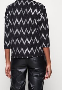 Svart och vit zigzag-mönstrad texturerad topp med trekvartslånga ärmar, bärs över svarta läderbyxor. Enkelt, avslappnat design.