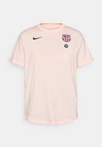 Svijetlopinkasti majica kratkih rukava izrađena od pamuka s okruglim izrezom, koja na prsima sadrži mornarsko plavi Nike logo i grb FC Barcelone.
