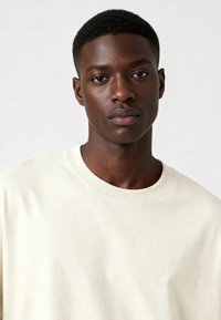 Gaiši pelēks kokvilnas T-krekls ar apaļu kakla izgriezumu un īsām piedurknēm, kas izceļas ar mīkstu tekstūru un minimālistisku dizainu.