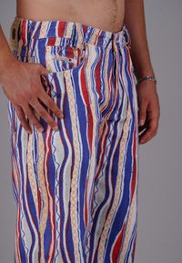 Gestreifte Hose mit rot, blau und orange Mustern. Leichter Stoff mit elastischem Bund und Seitentaschen.