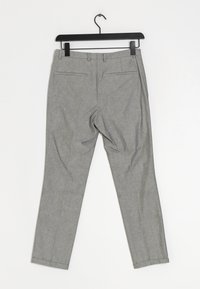 Šedé kalhoty s texturovanou tkaninou, se slim střihem, dvěma zadními kapsami a čistým lemem, visící na černém ramínku.
