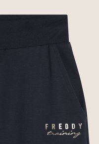 Pantalones de chándal azul marino con cinturilla acanalada, que cuentan con dos bolsillos laterales y un logo metálico dorado "FREDDY training" en la parte inferior de la pierna izquierda.