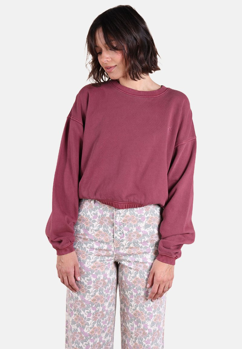Sweatshirt court bordeaux avec des manches oversize et des bords côtelés, associé à un pantalon à motif floral pastel. Texture douce semblable à celle du coton.