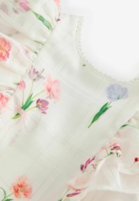 Weißes Stoffmuster mit floralen Motiven und transparenter Textur, mit rosa und lila Blumen, Rüschenausschnitten und dekorativer Spitze am Hals.