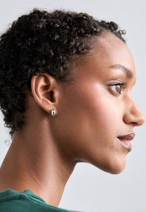 Orecchino a perno rotondo in argento su un modello con capelli neri corti e ricci, caratterizzato da una superficie liscia e un leggero splendore, su uno sfondo neutro.