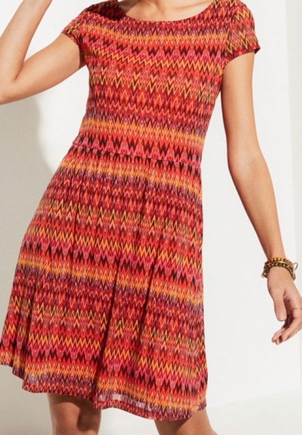 Kurzärmliges, rotes Kleid mit Zickzackmustern in Orange, Gelb und Rosa. Ausgestellter Rock und strukturierter Stoff. Einfacher runder Ausschnitt.