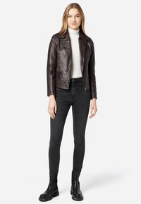 Bruine leren motorjack met een getailleerd ontwerp, puntige kraag, ritsluiting en twee voorkruiden, gecombineerd met zwarte skinny jeans en enkellaarzen.