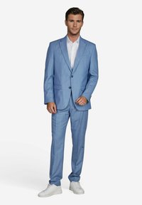 Lichtblauw pak met een getailleerde fit, voorzien van een notch-lapel en twee voorzakken. Gecombineerd met een wit shirt en witte sneakers.