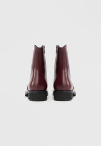 Botas de tornozelo em couro castanho-avermelhado com acabamento liso, zíperes laterais e salto preto empilhado, desenhadas com uma silhueta elegante.