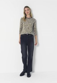 Langarmtop met een beige en zwart luipaardprint, gecombineerd met hoge zwarte jeans en zwarte enkellaarsjes.