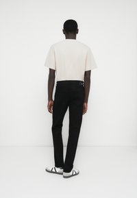 Bézs rövid ujjú póló, fekete slim-fit nadrág és fehér, fekete részletekkel díszített tornacipő. Simított textúra, minimalista dizájn.