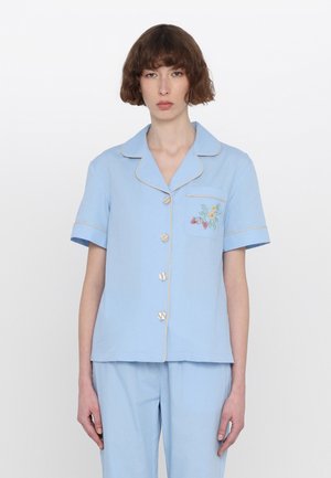 Lichtblauw pyjamapak in zachte stof, met korte mouwen, kraag en decoratieve borduursel op de zak met bloemmotieven. Vijf-knoop sluiting.