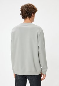 Ljusgrå sweatshirt med långa ärmar och rundad halsringning. Slät textur och ribbade muddar. Passar bekvämt med en avslappnad silhuett.