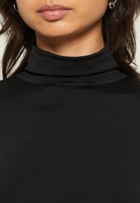 Svart høyhalset topp laget av glatt, elastisk stoff, med høy hals og en tettsittende design. Enkel, minimalistisk stil.